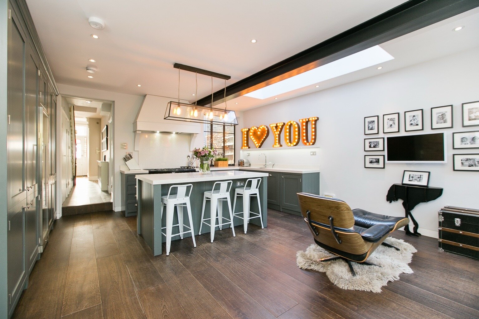 Open-plan kitchen in Brondesbury, London with a grey-green island, light worktops, rooflight and visible black steel beam